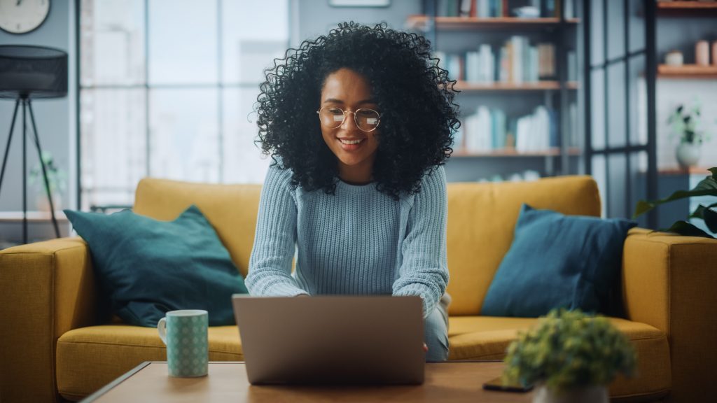 Portrait of a Beautiful Authentic Latina Female in a Stylish Cozy Living Room Using Laptop Computer at Home. She's Browsing the Internet and Checking Videos on Social Networks and Having Fun.